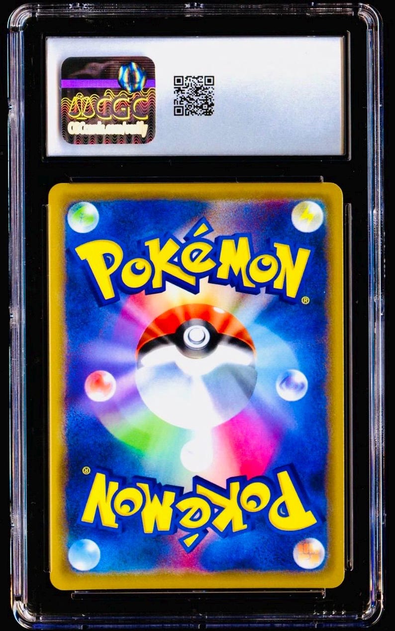Pu&ograve; includere: Una carta collezionabile Pok&eacute;mon valutata, racchiusa in un supporto di plastica trasparente. Il retro della carta presenta il logo Pok&eacute;mon in giallo e la parola "Pok&eacute;mon" in giallo. La carta ha uno sfondo blu con globi colorati.