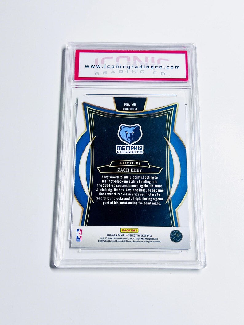 May include: A graded Zach Edey basketball card from the Memphis Grizzlies, encased in a clear protective holder. The card features the Grizzlies logo and player information. The top of the holder has a red and white label with the website address.