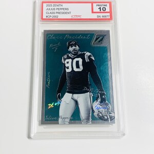 May include: A graded 2023 Zenith Julius Peppers Class President trading card. The card features a player in a black and blue uniform with the number 90. The card is graded Pristine 10 and encased in a protective holder. The card has the text "Class President" and "Panthers".