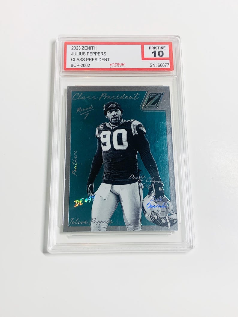May include: A graded 2023 Zenith Julius Peppers Class President trading card. The card features a player in a black and blue uniform with the number 90. The card is graded Pristine 10 and encased in a protective holder. The card has the text "Class President" and "Panthers".