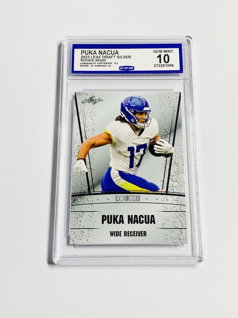 May include: A graded Puka Nacua rookie card. The card features a player in a blue and white uniform, with the number 17. The card is labeled "2023 Leaf Draft Silver" and is graded as "Gem Mint 10". The card is encased in a clear protective holder.