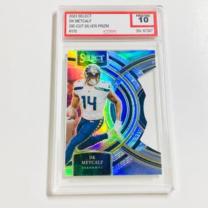 May include: A 2023 Select DK Metcalf Die-Cut Silver Prizm trading card, graded Pristine 10. The card features a player in a Seahawks uniform, with the number 14. The card is encased in a clear protective holder.