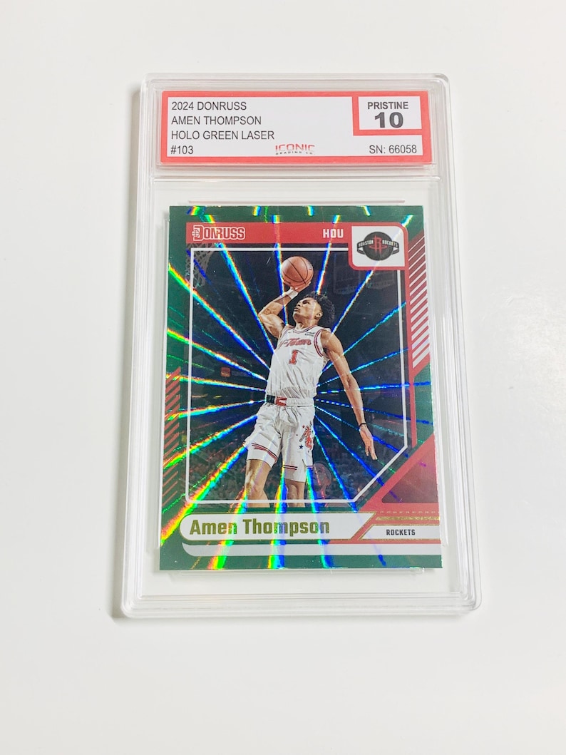 Op de afbeelding: Een basketbal trading card met Amen Thompson in actie, met een groen holografisch ontwerp. De kaart is beoordeeld met Pristine 10 en zit in een beschermende houder. De kaart leest "2024 Donruss" en "Holo Green Laser".