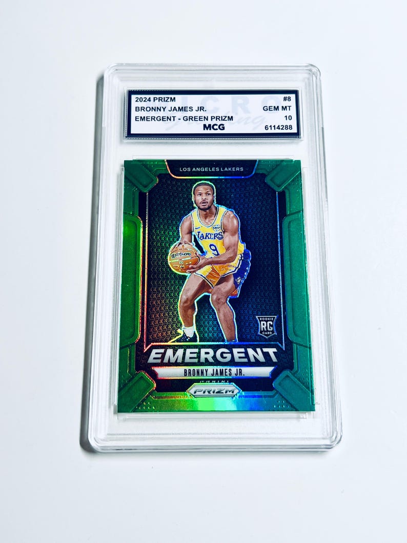 May include: A 2024 Prizm basketball card featuring Bronny James Jr. The card is graded GEM MT 10 and has a green prism design. The card features the text "EMERGENT" and "LOS ANGELES LAKERS".
