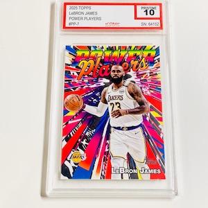 K&ouml;nnte beinhalten: Eine 2025 Topps LeBron James Power Players Sammelkarte, bewertet mit Pristine 10, in einer Schutzh&uuml;lle. Die Karte zeigt LeBron James im Lakers-Trikot vor einem leuchtenden, farbenfrohen Hintergrund. Der Text auf der Karte enth&auml;lt "Power Players" und "LeBron James".