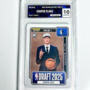 May include: A graded Cooper Flagg rookie card from the 2025 Panini Instant NBA series. The card features a photo of Flagg in a suit holding a basketball. The card is graded a 10 GEM MT. The card is encased in a clear protective holder.