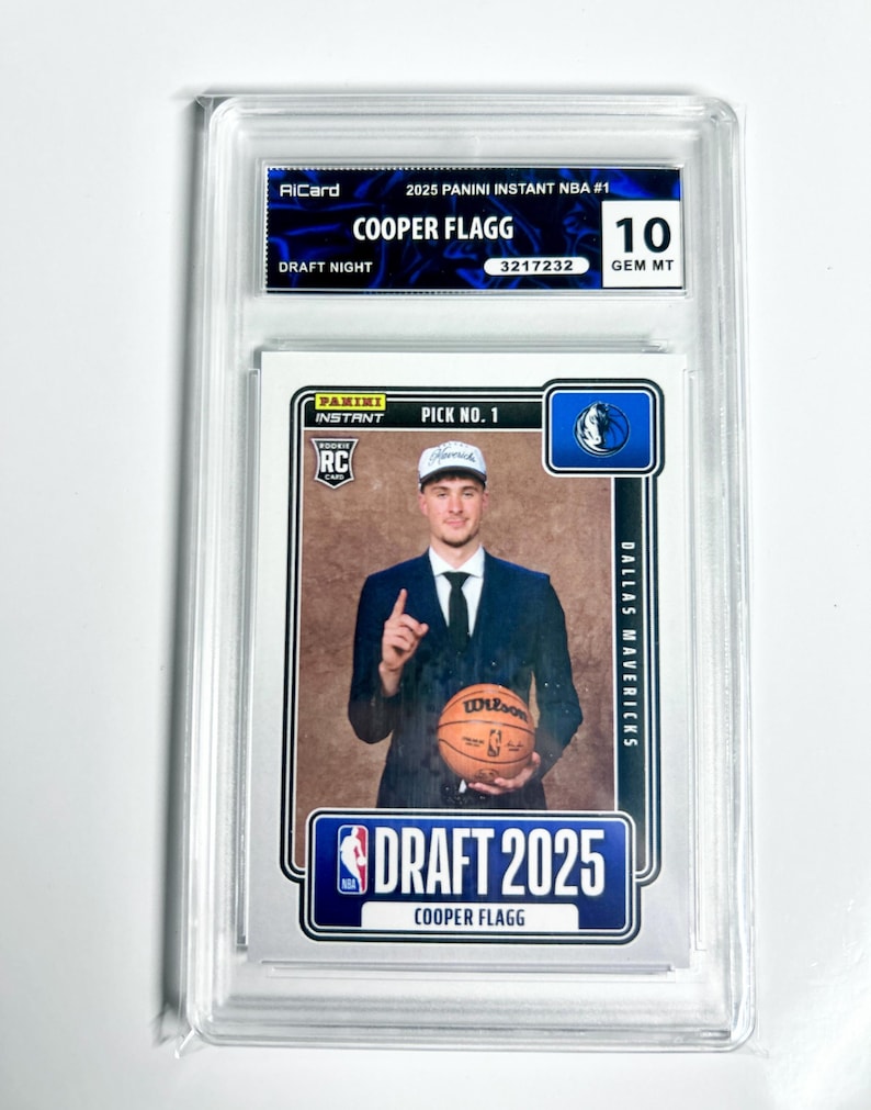 May include: A graded Cooper Flagg rookie card from the 2025 Panini Instant NBA series. The card features a photo of Flagg in a suit holding a basketball. The card is graded a 10 GEM MT. The card is encased in a clear protective holder.