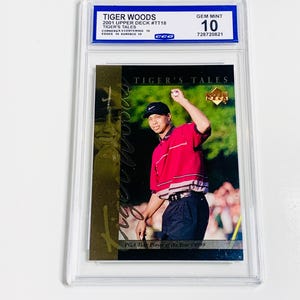 Pu&ograve; includere: Una carta collezionabile di Tiger Woods valutata del set Upper Deck 2001, con una foto di Woods con camicia rossa e pantaloni neri. La carta &egrave; valutata Gem Mint 10 da CCG, con il testo "TIGER'S TALES".
