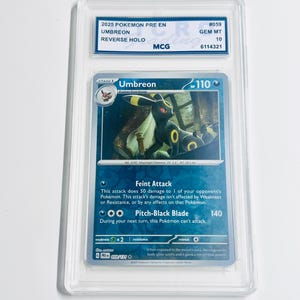 May include: A graded Pokémon card featuring Umbreon, a dark-type Pokémon. The card is encased in a clear protective holder with a label indicating it's a Reverse Holo, graded Gem Mint 10. The card's text includes attack descriptions and the number 059.
