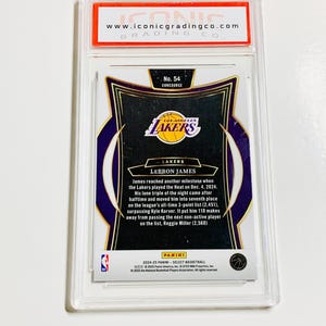 May include: A basketball trading card encased in a clear plastic holder. The card features the Los Angeles Lakers logo and text that reads "LEBRON JAMES." The card is graded by Iconic Grading Co.