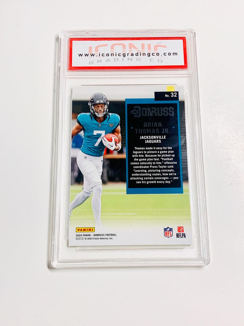 May include: A graded Panini Donruss football card featuring Brian Thomas Jr. of the Jacksonville Jaguars. The card is encased in a clear protective holder with the Iconic Grading Co. logo at the top. The player is wearing a teal jersey with the number 7.