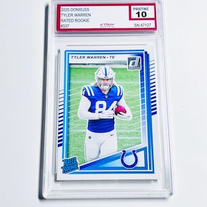 Puede incluir: Una tarjeta de f&uacute;tbol de Tyler Warren calificada del conjunto Donruss 2025. La tarjeta presenta a Warren con su uniforme de los Colts de Indian&aacute;polis, sosteniendo un bal&oacute;n de f&uacute;tbol. La tarjeta est&aacute; etiquetada como "Rated Rookie" y est&aacute; calificada como "Pristine 10".