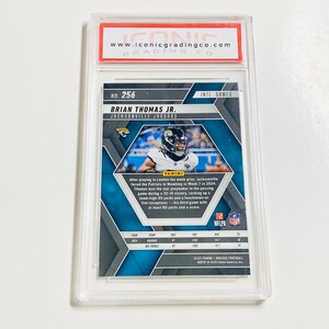 May include: A graded Brian Thomas Jr. Jacksonville Jaguars football card, encased in a clear protective holder. The card features a mosaic design and includes text about the player's performance. The top of the holder has a red and white label with the website address.
