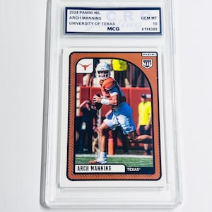 K&ouml;nnte beinhalten: Eine 2024 Panini NIL Arch Manning University of Texas Sammelkarte in einer durchsichtigen Kunststoffh&uuml;lle. Die Karte zeigt ein Foto eines Footballspielers in einem orangefarbenen Trikot und wei&szlig;en Shorts, mit dem aufgedruckten Text Arch Manning und Texas.