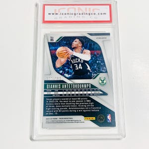 May include: A basketball trading card featuring Giannis Antetokounmpo in a Bucks uniform. The card is graded and encased in a protective holder. The card's details include player stats, the Prizm logo, and the Panini logo.