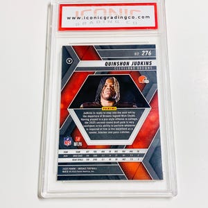 Pu&ograve; includere: Una carta di football di Quinshton Judkins dei Cleveland Browns, valutata e racchiusa in un supporto di plastica trasparente. La carta presenta un design a mosaico con una foto del giocatore e testo con il suo nome, la squadra e le statistiche.