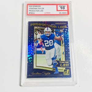 May include: A 2022 Donruss Jonathan Taylor Production Line trading card, graded Pristine 10. The card features a photo of Jonathan Taylor in a blue and white uniform. The card is encased in a clear protective holder.