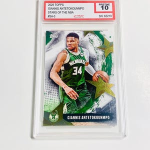 May include: A 2025 Topps basketball card featuring Giannis Antetokounmpo in a Milwaukee Bucks uniform. The card is graded Pristine 10 and encased in a protective holder. The card's text includes "STARS OF THE NBA" and "#SA-3".