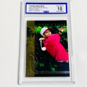 May include: A Tiger Woods 2001 Upper Deck #TT10 trading card, graded GEM MINT 10 by CCO. The card features a photo of Tiger Woods in a red shirt and white hat. The card is encased in a clear protective holder.