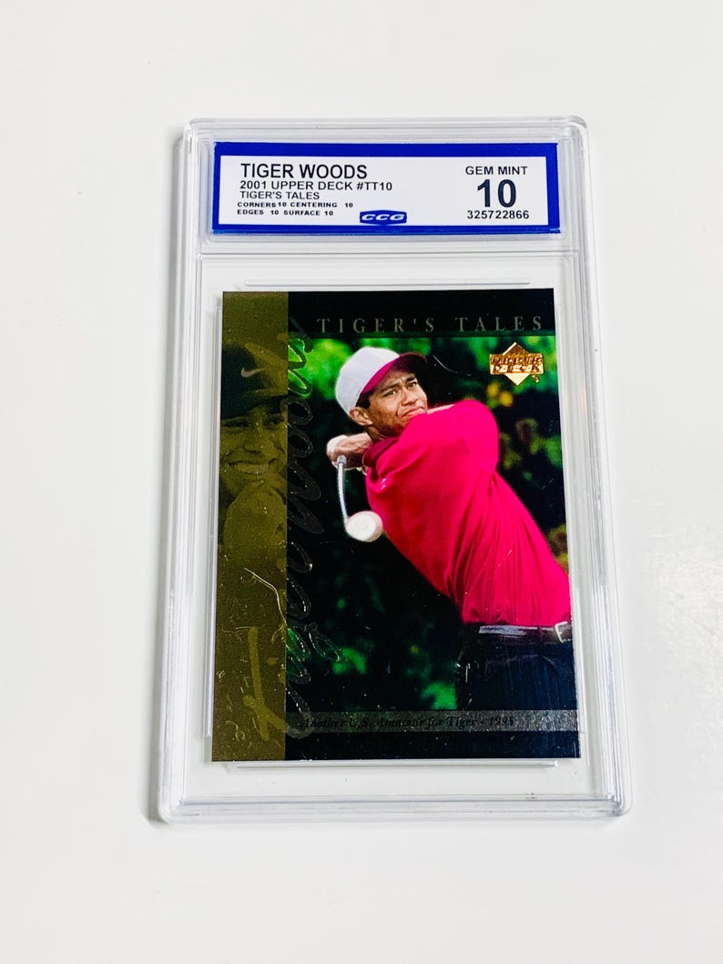 May include: A Tiger Woods 2001 Upper Deck #TT10 trading card, graded GEM MINT 10 by CCO. The card features a photo of Tiger Woods in a red shirt and white hat. The card is encased in a clear protective holder.