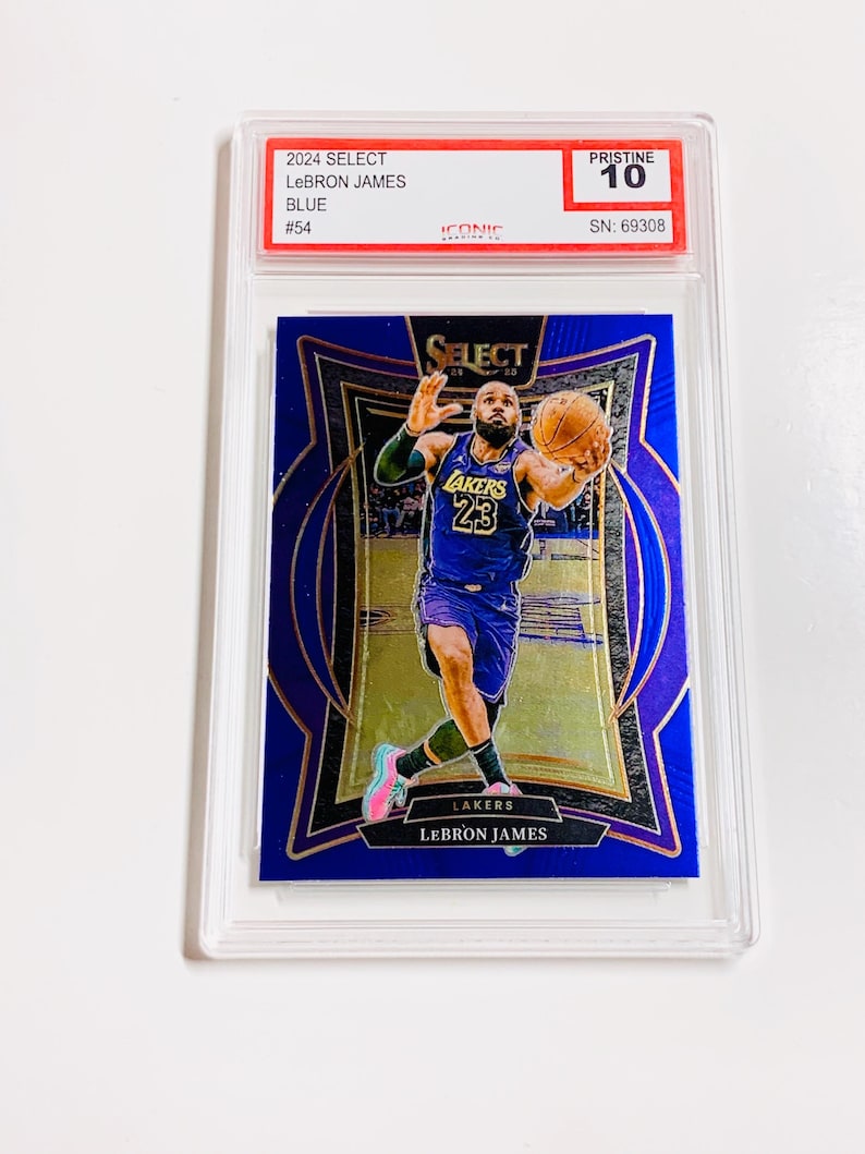 May include: A blue 2024 Select LeBron James basketball card, graded Pristine 10, encased in a protective holder. The card features LeBron James in a Lakers uniform, with gold accents and the Lakers logo.