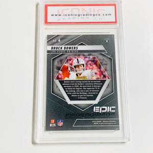 以下が含まれることがあります： ラスベガス・レイダースのブロック・バワーズ選手のフットボールカード。透明なケースに収められ、評価されています。カードにはPaniniのロゴと「EPIC PERFORMERS」の文字があります。評価会社のウェブサイトが上部に表示されています。