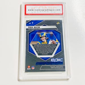 May include: A Puka Nacua Los Angeles Rams football card, graded and encased in a protective holder. The card features a photo of the player in action, with the Panini logo and the text "EPIC PERFORMERS". The card is from the 2025 Panini Mosaic Football collection.