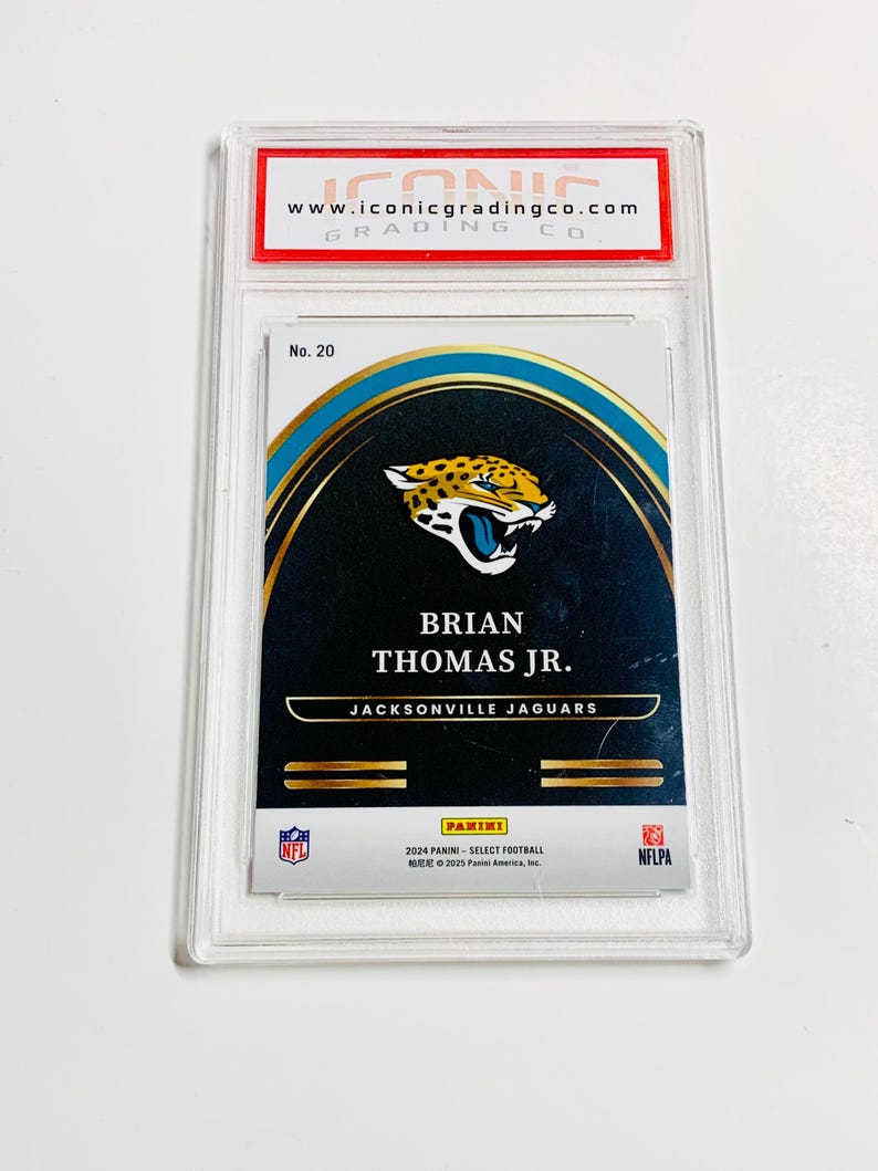 May include: A graded trading card featuring Brian Thomas Jr. of the Jacksonville Jaguars. The card is encased in a clear plastic holder with the "ICONIC GRADING CO" logo at the top. The card has a gold, black, and teal design with the Panini logo.