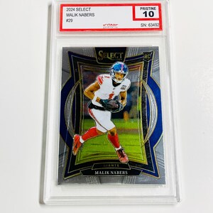 Puede incluir: Una tarjeta coleccionable de f&uacute;tbol con Malik Nabers con el uniforme de los Giants. La tarjeta est&aacute; calificada como Pristine 10 y est&aacute; dentro de un soporte protector. Se puede leer el texto "2024 SELECT MALIK NABERS #29" y "GIANTS MALIK NABERS".