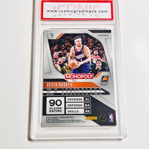 Pu&ograve; includere: Una carta collezionabile di basket racchiusa in un supporto di plastica trasparente. La carta presenta Devin Booker dei Suns, con il marchio "MONOPOLY" e "PRIZM". La carta mostra le statistiche del giocatore e una valutazione del giocatore di 90.