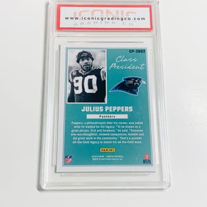 May include: A football trading card featuring Julius Peppers of the Carolina Panthers. The card is encased in a protective holder and includes the text "Class President" and the Panini logo. The card has a teal and black color scheme.