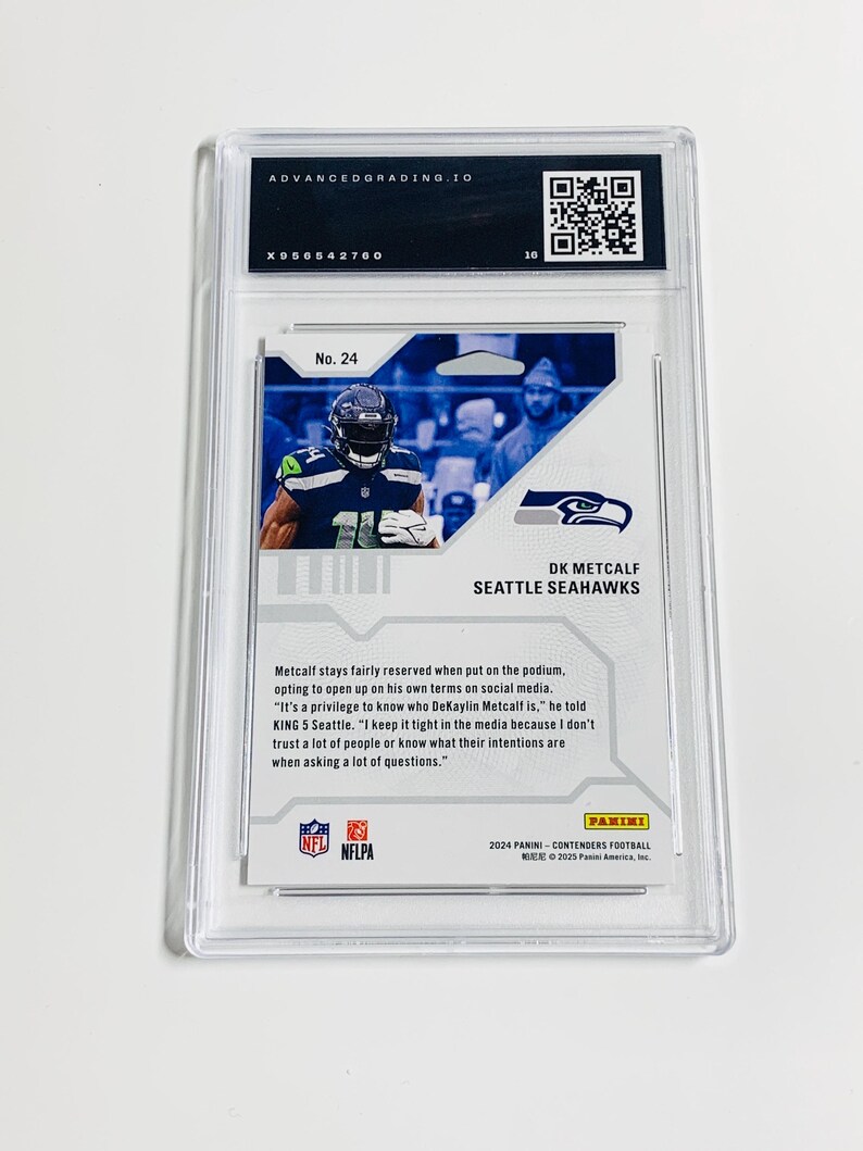 K&ouml;nnte beinhalten: Eine bewertete DK Metcalf Seattle Seahawks Footballkarte in einer Schutzh&uuml;lle. Die Karte zeigt ein Foto des Spielers in seiner Uniform. Die Karte ist mit der Nummer 24 versehen und enth&auml;lt Text &uuml;ber den Spieler.