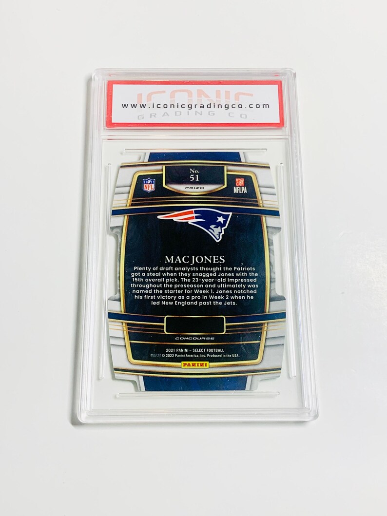 May include: A graded Mac Jones football card from the 2021 Panini Select Football series. The card is encased in a clear plastic holder with a red and white label from Iconic Grading Co. The card features the NFL and NFLPA logos.