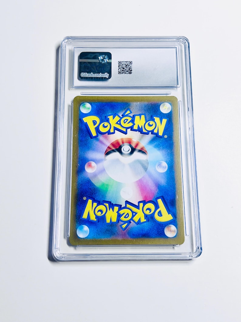 Op de afbeelding: Een beoordeelde Pok&eacute;mon-verzamelkaart in een doorzichtige plastic houder. De achterkant van de kaart is blauw met het Pok&eacute;mon-logo en een Pok&eacute; Ball-ontwerp. De houder heeft een label met de tekst "ggcards.com/verify".