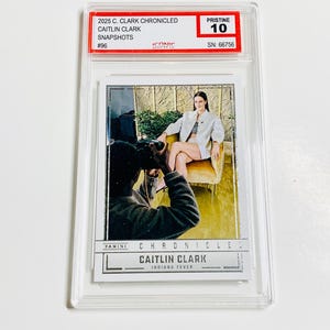 May include: A Caitlin Clark trading card, graded Pristine 10, in a clear protective case. The card shows a photo of Caitlin Clark and the text "2025 C. Clark Chronicled Snapshots #96". The card is from the Indiana Fever.