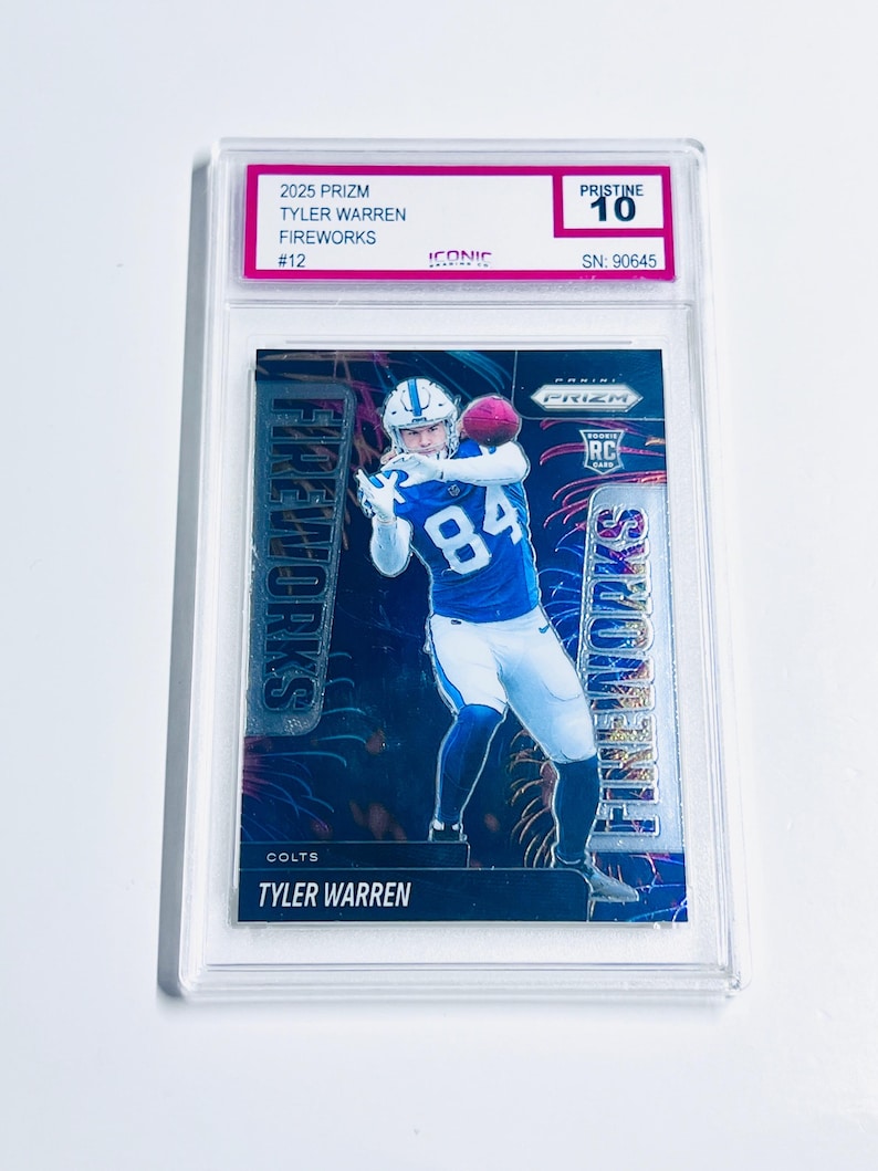 Puede incluir: Una tarjeta de f&uacute;tbol con Tyler Warren en uniforme azul y blanco, atrapando un bal&oacute;n rosa. La tarjeta est&aacute; etiquetada como "2025 Prizm Fireworks" y est&aacute; calificada como "Pristine 10". La tarjeta est&aacute; dentro de un soporte protector transparente.