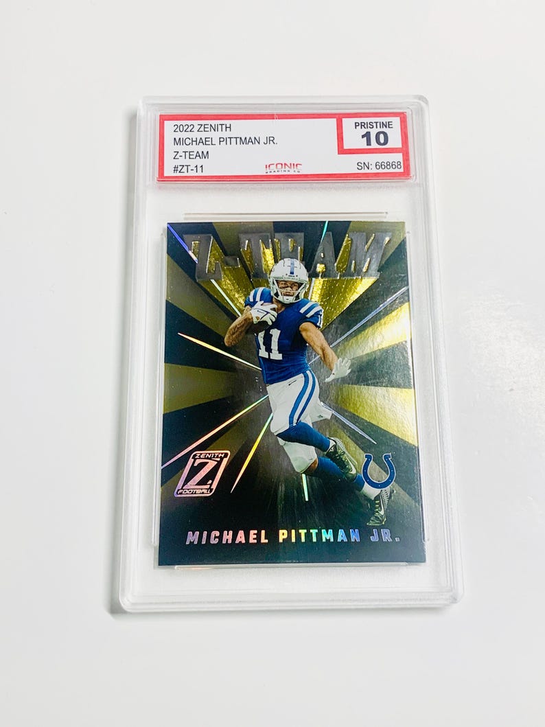May include: A 2022 Zenith Michael Pittman Jr. Z-Team football trading card, graded Pristine 10, encased in a protective holder. The card features a player in a blue and white uniform against a gold and black background.
