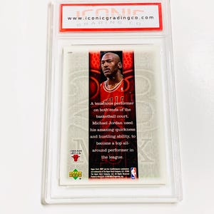 May include: A graded Upper Deck basketball card featuring Michael Jordan in a Chicago Bulls uniform. The card is encased in a clear plastic holder with the text "www.iconicgradingco.com" visible at the top. The card text describes Jordan's performance.