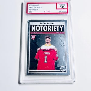 Pode incluir: Um cart&atilde;o colecion&aacute;vel de EMEKA EGBUKA com a palavra "NOTORIETY". O cart&atilde;o mostra um jogador segurando uma camisa vermelha com o n&uacute;mero 1. O cart&atilde;o &eacute; classificado como "PRISTINE 10" e est&aacute; em um suporte protetor.