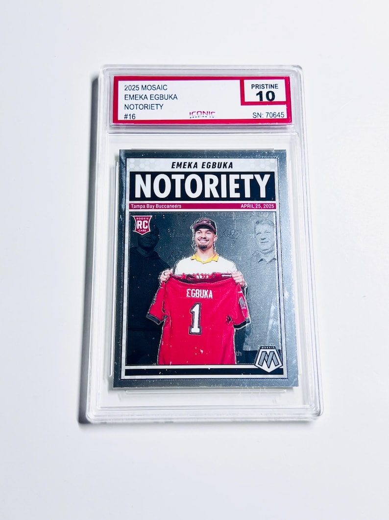Pode incluir: Um cart&atilde;o colecion&aacute;vel de EMEKA EGBUKA com a palavra "NOTORIETY". O cart&atilde;o mostra um jogador segurando uma camisa vermelha com o n&uacute;mero 1. O cart&atilde;o &eacute; classificado como "PRISTINE 10" e est&aacute; em um suporte protetor.