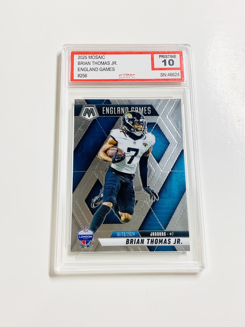 May include: A football trading card featuring Brian Thomas Jr. in a Jacksonville Jaguars uniform. The card is encased in a protective holder and includes the text "2025 Mosaic England Games" and "Pristine 10".
