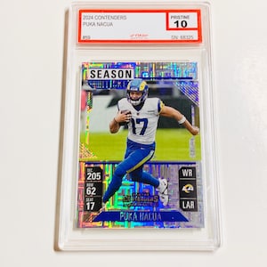 May include: A football trading card featuring Puka Nacua in a Los Angeles Rams uniform. The card is graded Pristine 10 and includes the text "2024 Contenders" and "Season Ticket". The card is encased in a clear protective holder.