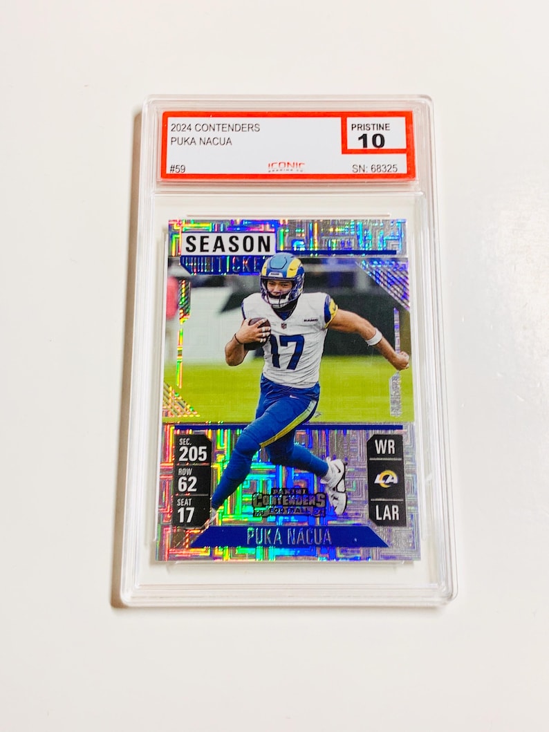 May include: A football trading card featuring Puka Nacua in a Los Angeles Rams uniform. The card is graded Pristine 10 and includes the text "2024 Contenders" and "Season Ticket". The card is encased in a clear protective holder.