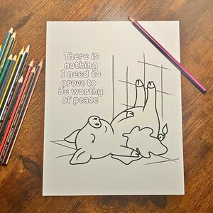 May include: A coloring page with a cartoon pig illustration, the text "There is nothing I need to prove to be worthy of peace", and a collection of colored pencils. A pink and purple pencil rests on the page.