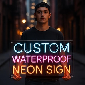 Puede incluir: Un letrero de neón rectangular transparente con las palabras "CUSTOM WATERPROOF NEON SIGN" en azul, rosa y naranja. El letrero lo sostiene una persona con una camiseta negra y una gorra negra. El fondo es una escena callejera borrosa.