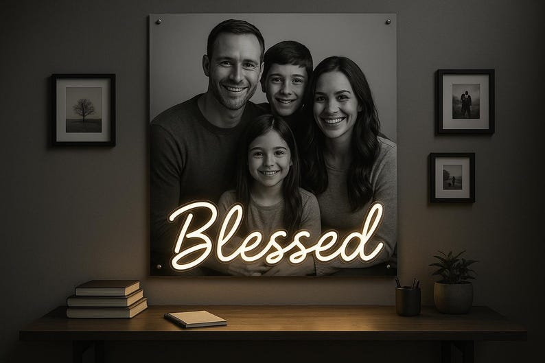 May include: A black and white family portrait with the word "Blessed" in neon script. The portrait is mounted on a wall, with framed pictures and a desk with books and a plant in front.