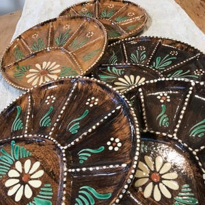 May include: Set of six brown ceramic divided serving plates with white and green floral designs. Each plate has a scalloped edge and is divided into sections.