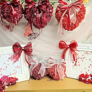 May include: Valentine's Day decorations in red and white, including heart-shaped ornaments, picture frames, and bows. The display also features decorative butterflies and floral arrangements, creating a romantic atmosphere.