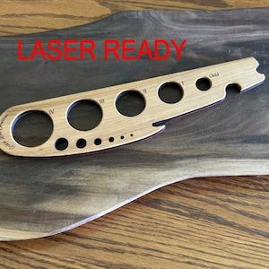 May include: A light-colored wooden gauge with multiple circular openings of varying sizes, labeled with Roman numerals and the word "Child." The text "Laser Ready" is in red. The gauge is on a dark wooden surface.