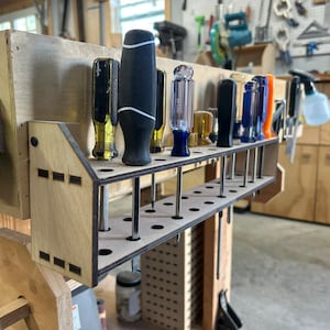 May include: A wooden tool organizer with a row of holes for holding screwdrivers. The organizer is mounted on a wall and has a variety of screwdrivers in different colors and sizes.